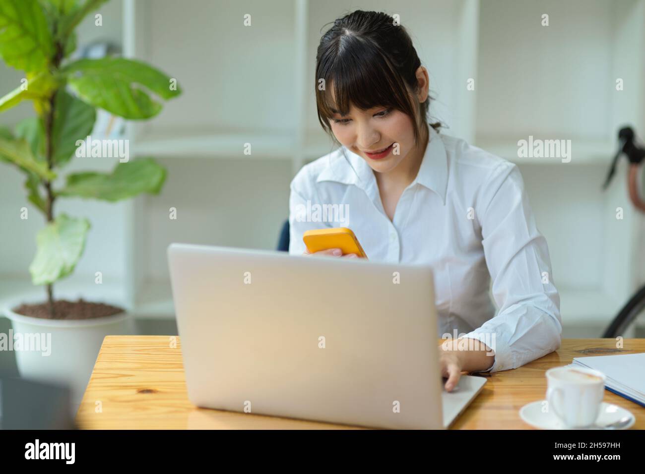 Female college student using smartphone for searching an informations while doing assignment on laptop. Stock Photo