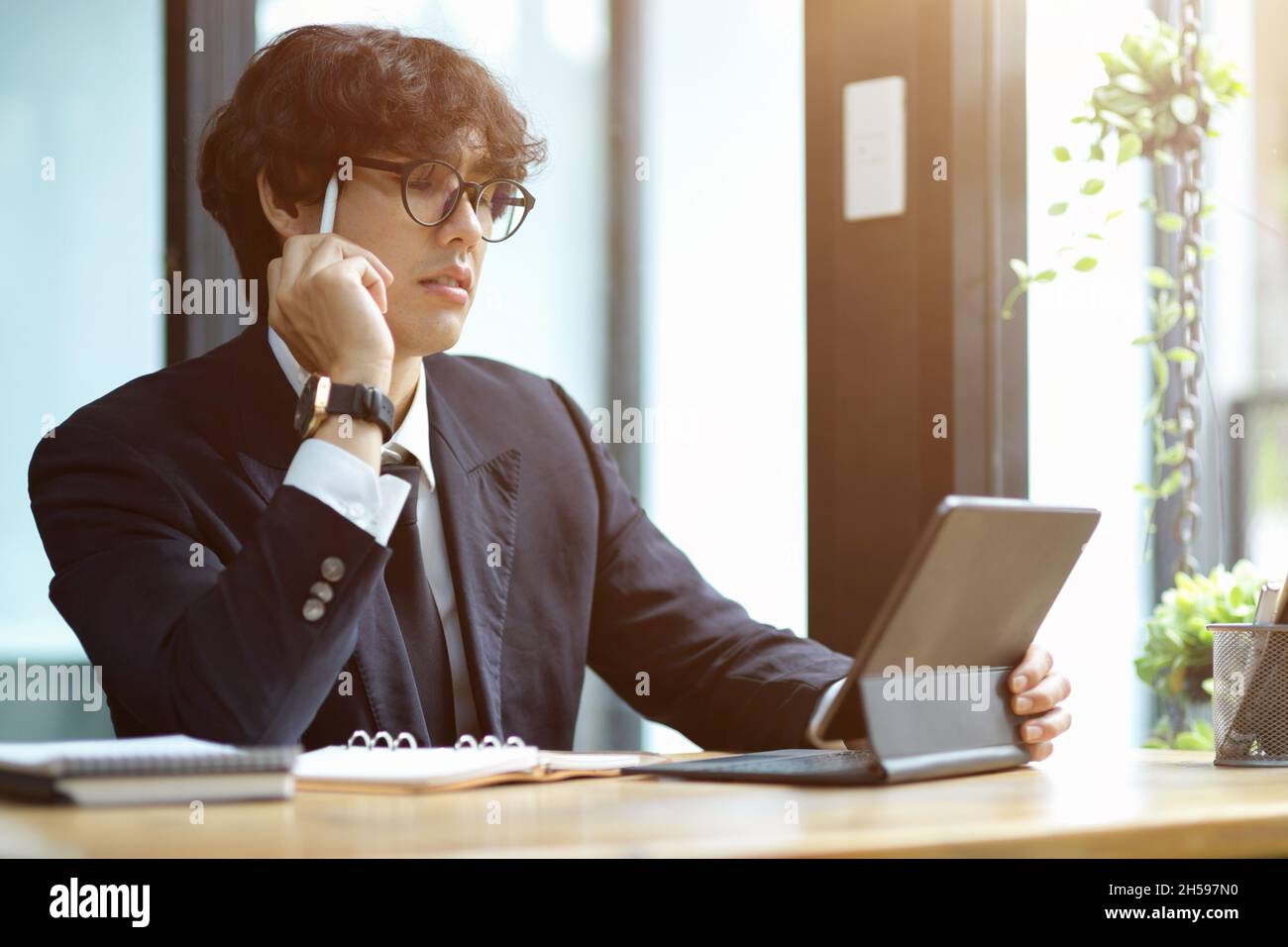 Focused young businessman working and pensive thinking on his project assignment while using tablet computer. Stock Photo