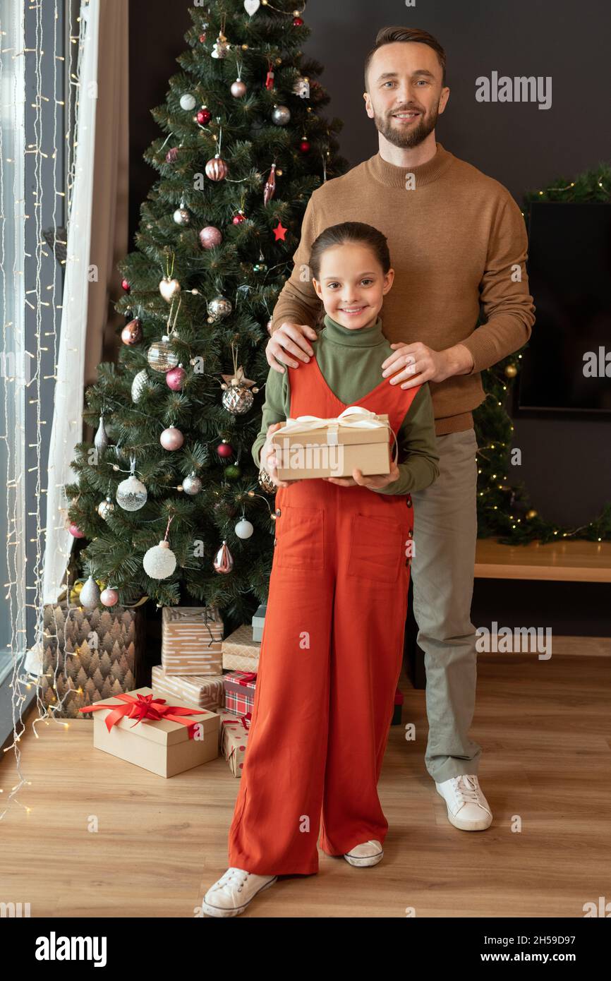 Portrait of happy middle-aged father in sweater holding hands on daughters shoulder against Christmas tree at home Stock Photo