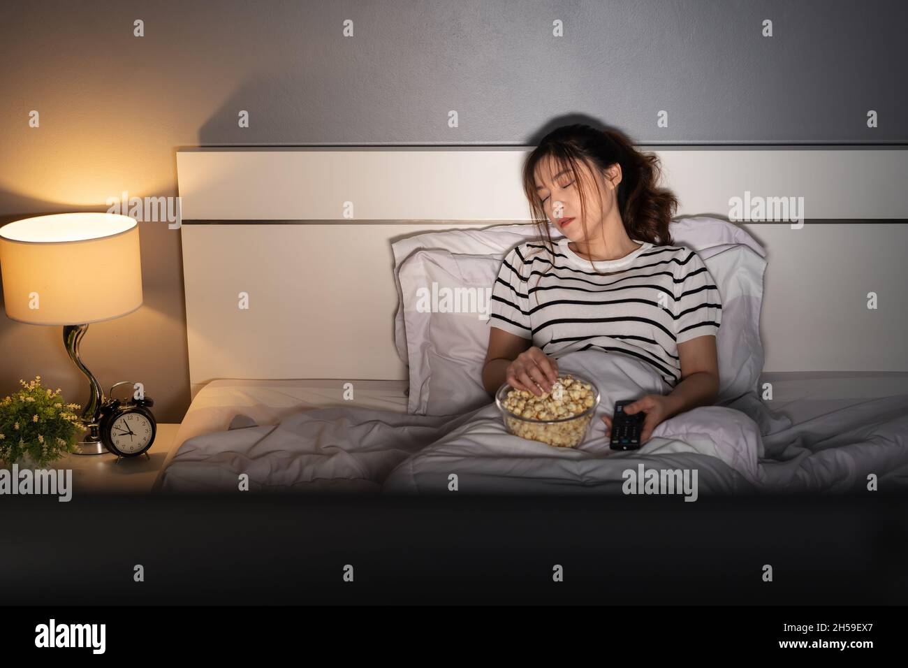 young woman sleeping while watching tv on a bed at night Stock Photo