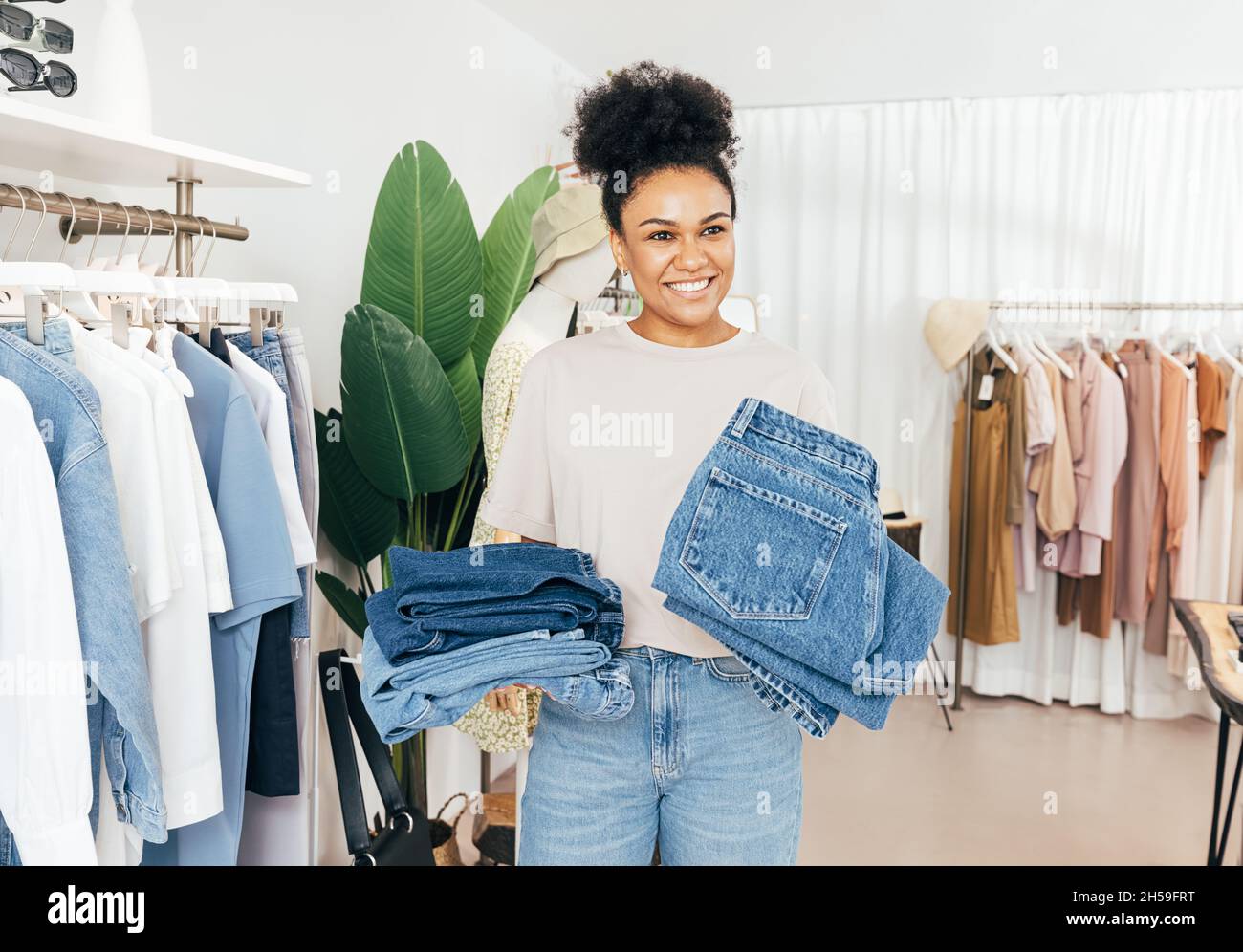 Cheerful saleswoman standing in clothing store with two piles of jeans  Stock Photo - Alamy