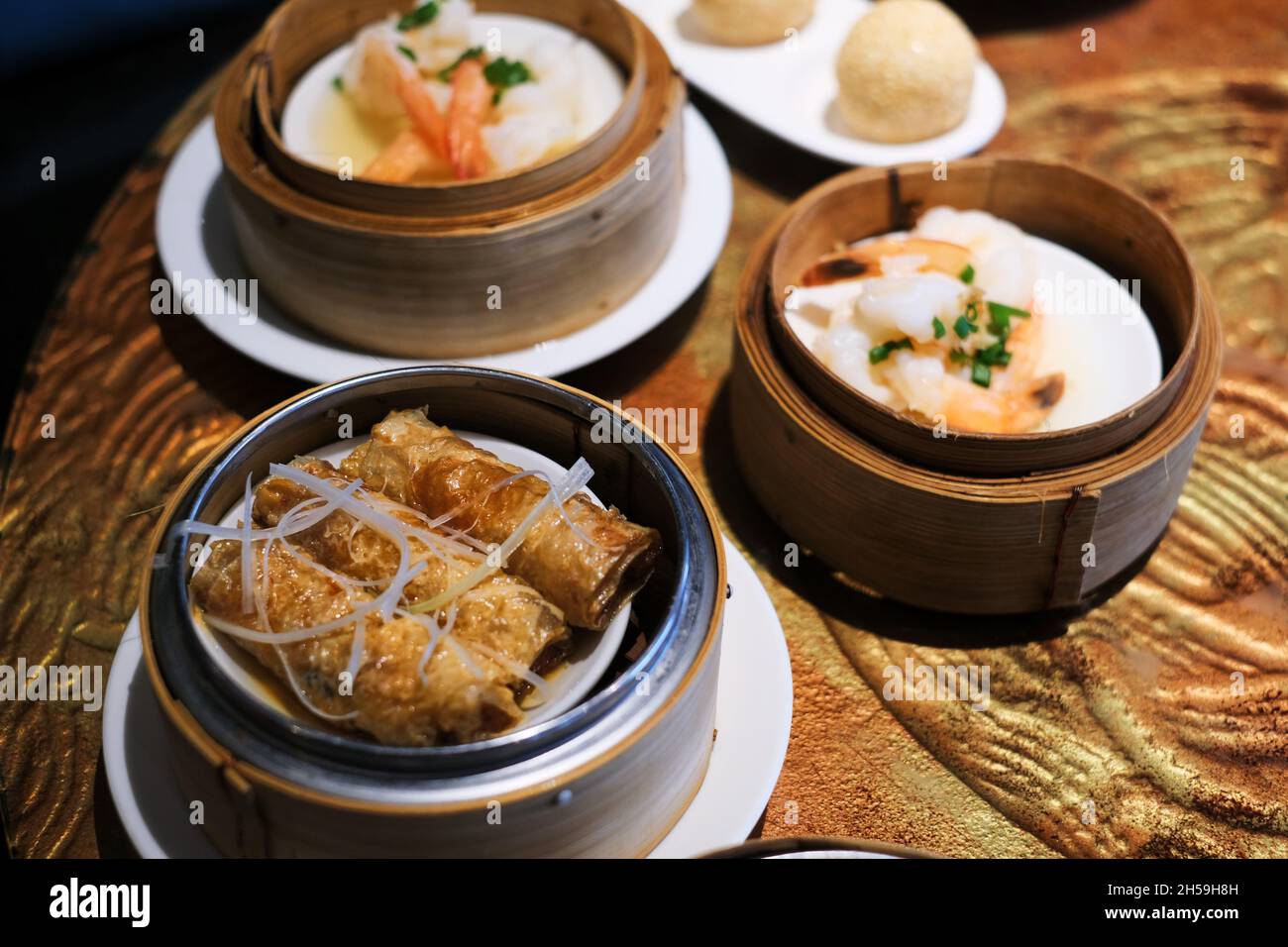 An assorted dishes of fried and steamed dim sum or Chinese dumpling, served in round bamboo steamers on a wooden table at a Chinese restaurant. Stock Photo