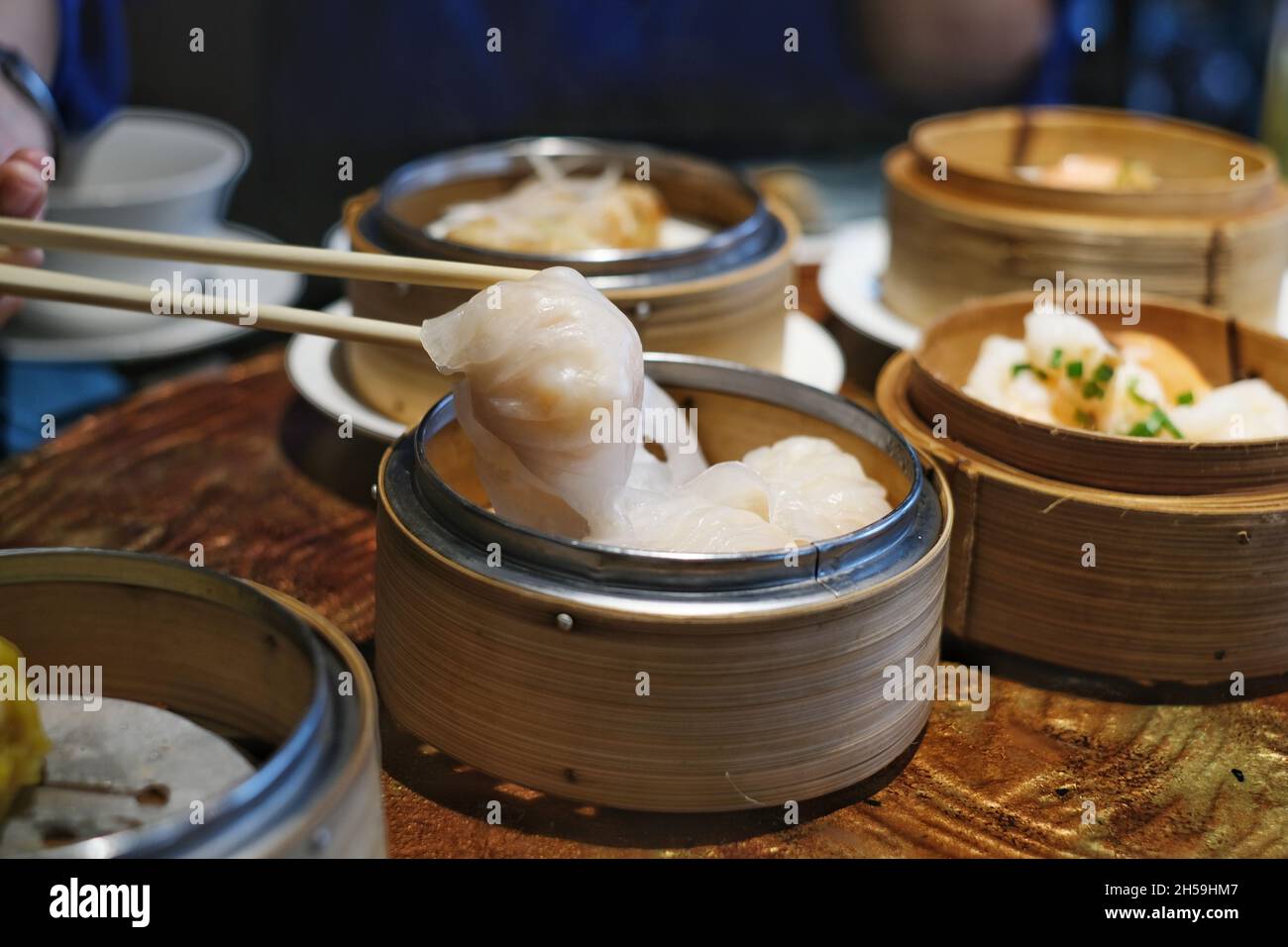 A close-up picture of bamboo chopsticks picking up white white Chinese stuffed steamed dumpling, also known as dim sum from a round bamboo basket on a Stock Photo