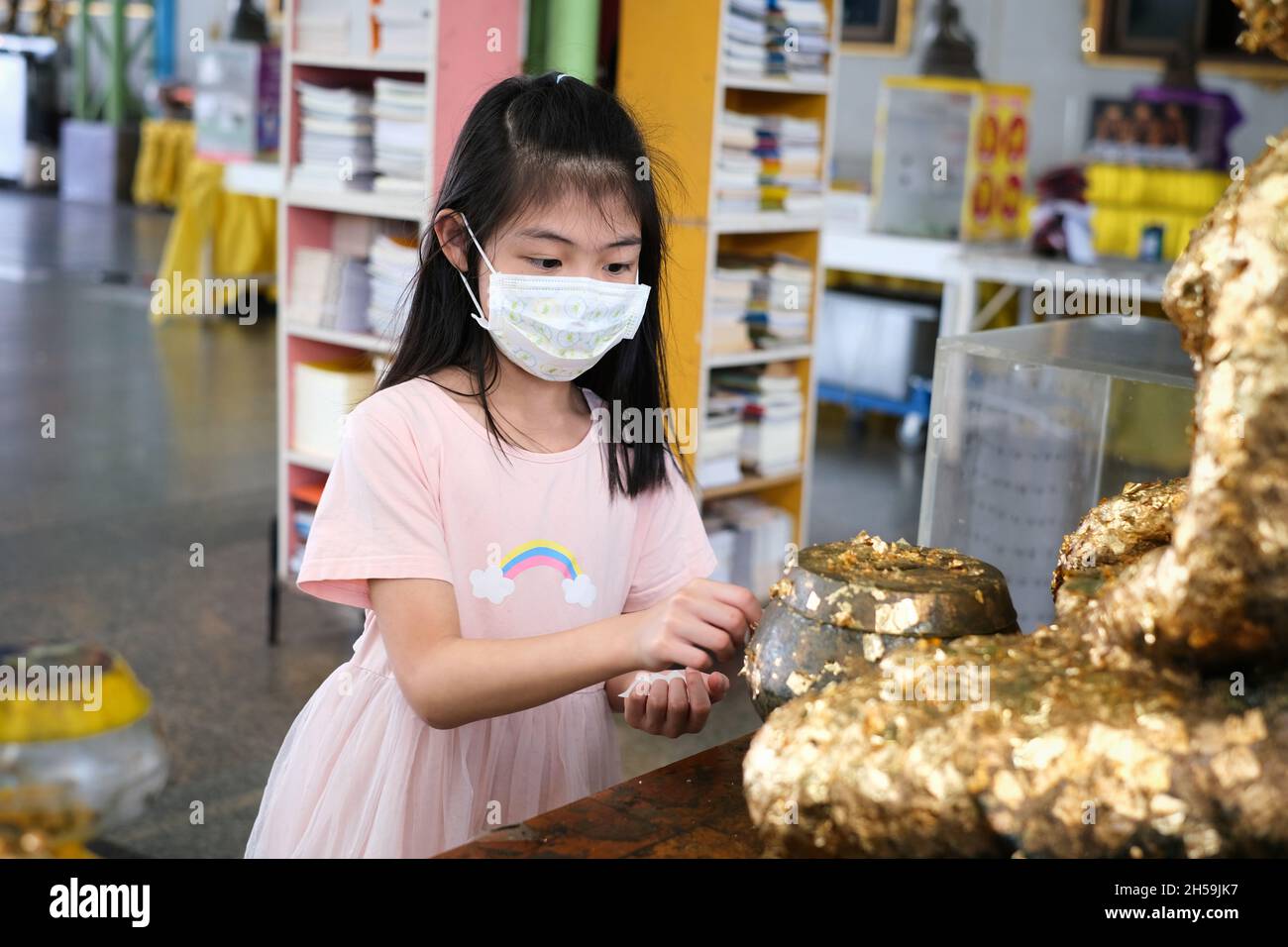 An Asian woman is gilding thin gold leaf on a buddha statue at a Thai temple in Thailand. Attach or sticking gold leaf on the arm of Buddha statue. Stock Photo