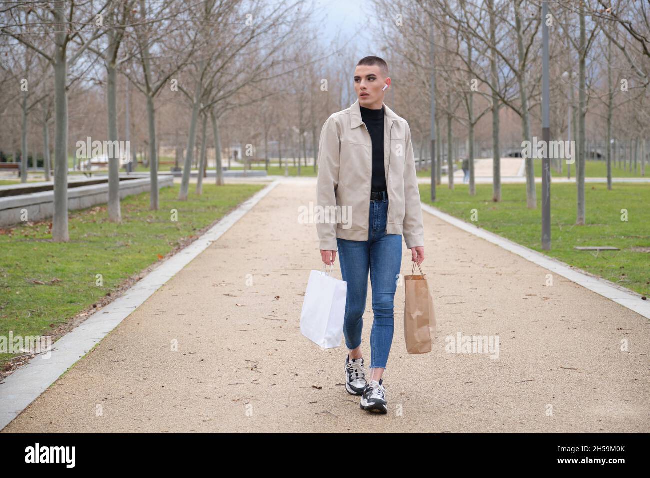 Young man wearing make up walking with shopping bags and listening music. Stock Photo