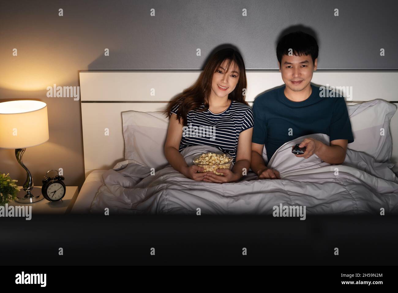 happy young couple watching TV on a bed at night Stock Photo