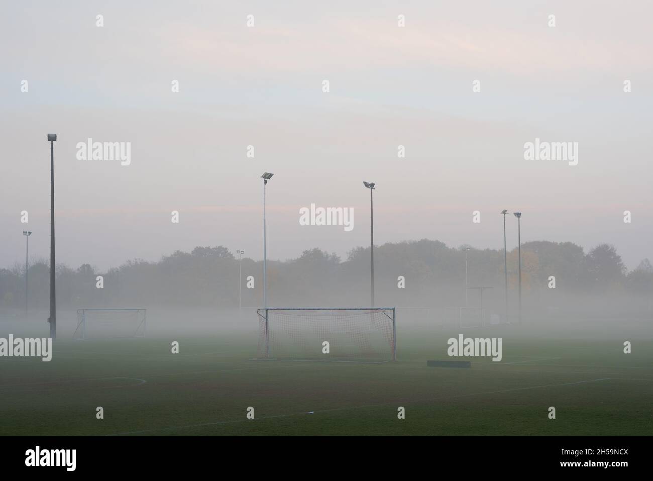 Empty and deserted soccer field in suburban area with goals and flood light poles on grey overcast day with fog and mist Stock Photo