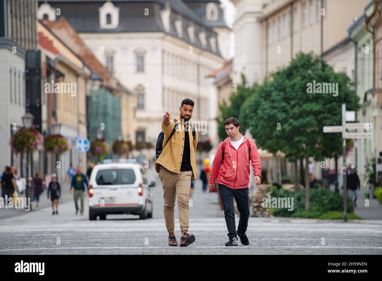 Young man with Down syndrome and his mentoring friend walking and talking outdoors Stock Photo