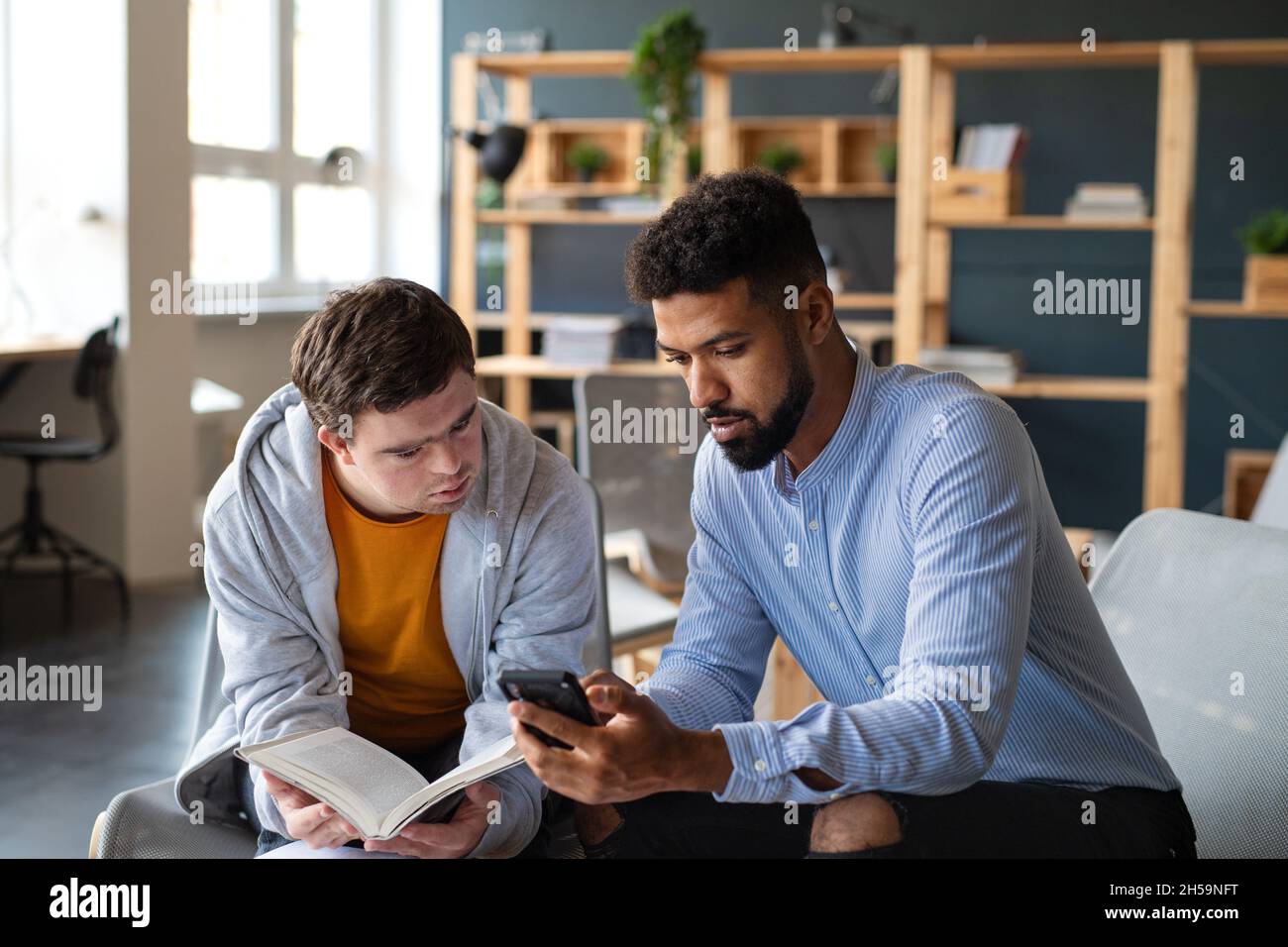 Young man with Down syndrome and his tutor studying indoors at school. Stock Photo