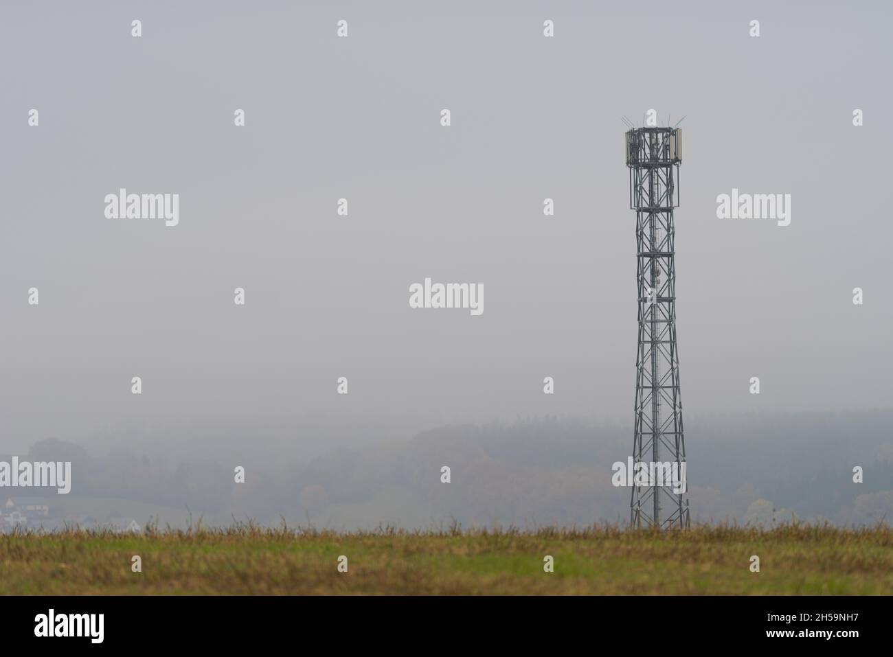 Mobile cell tower antenna mast providing mobile internet connection for rural area standing on empty barren field on grey overcast dark moody day Stock Photo