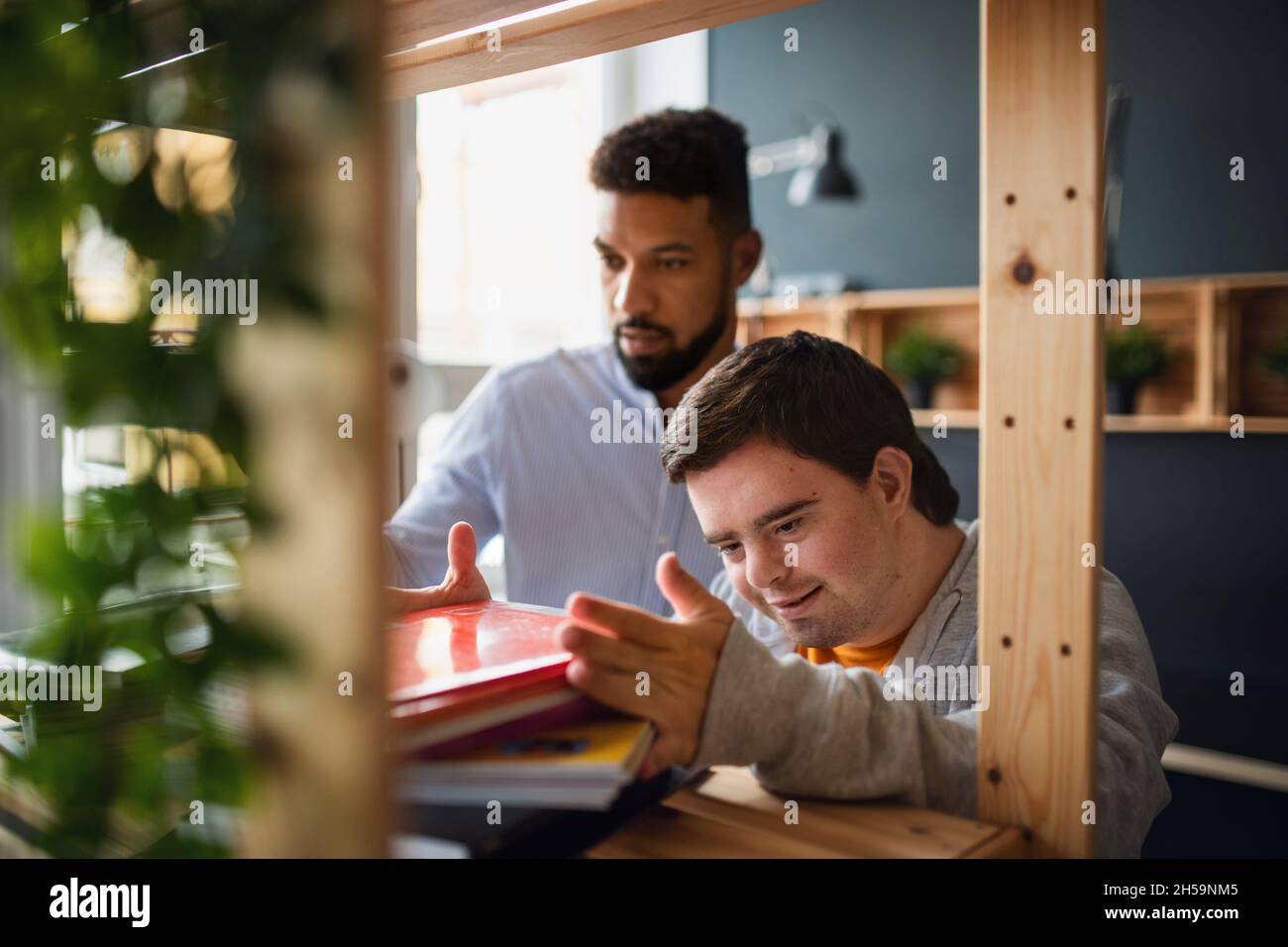 Young happy man with Down syndrome and his tutor indoors at staffroom. Stock Photo