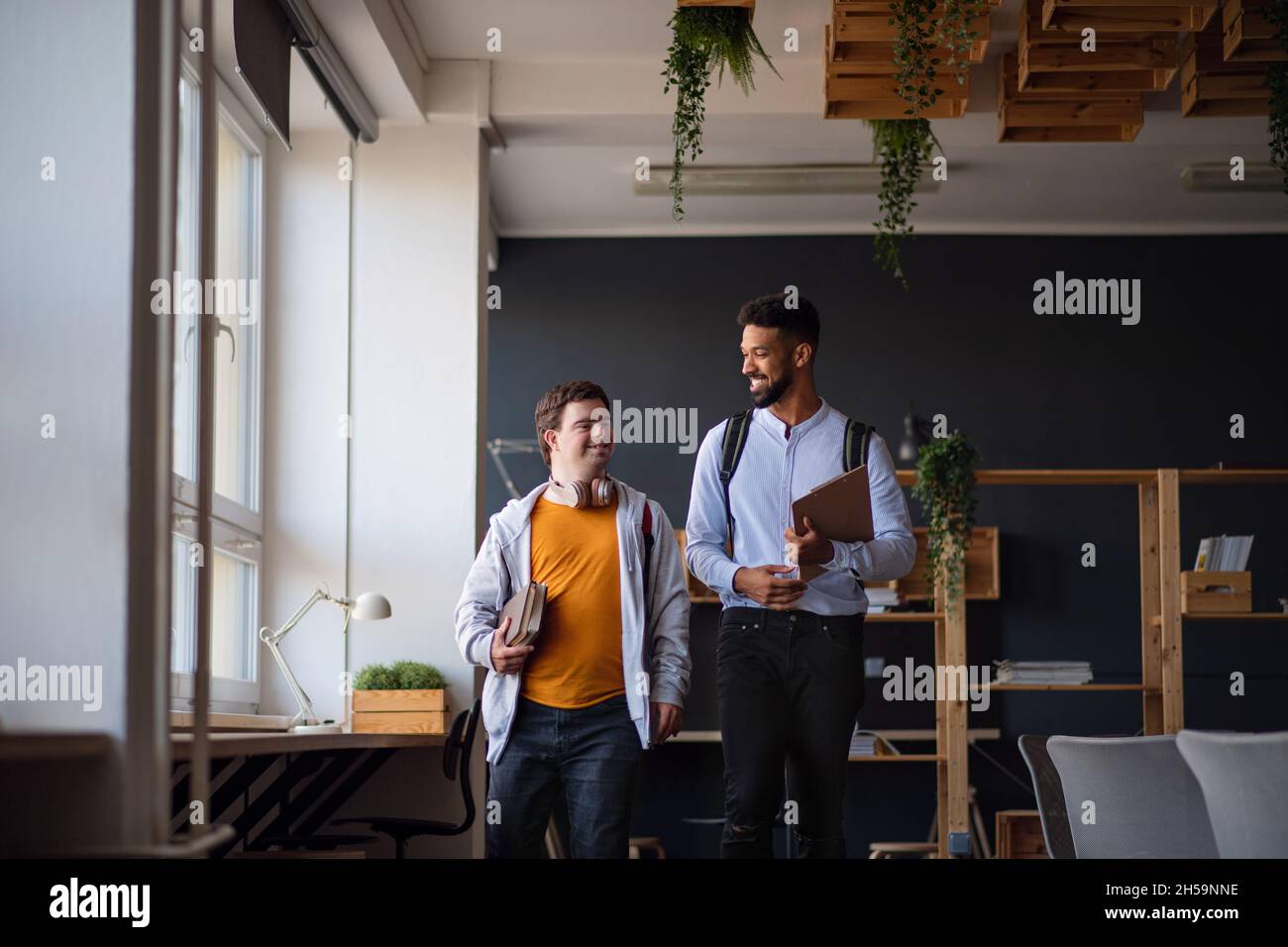 Young man with Down syndrome and his tutor looking at each other indoors at school Stock Photo