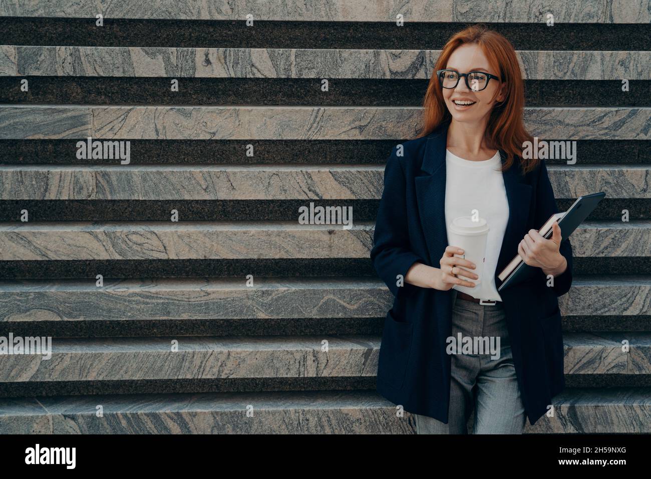 Woman dressed formally drinks takeaway coffee holds digital tablet and ...