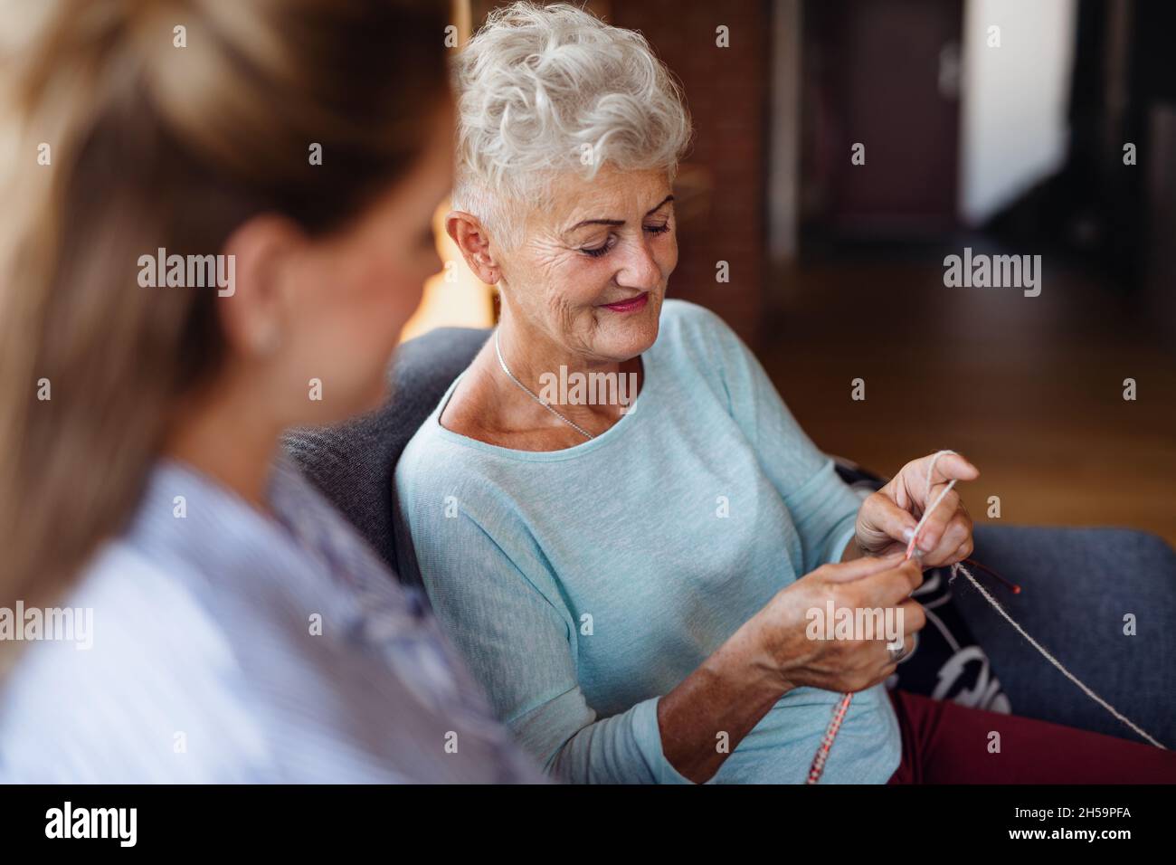 Happy senior woman sitting on sofa and learning to knit her adult ...