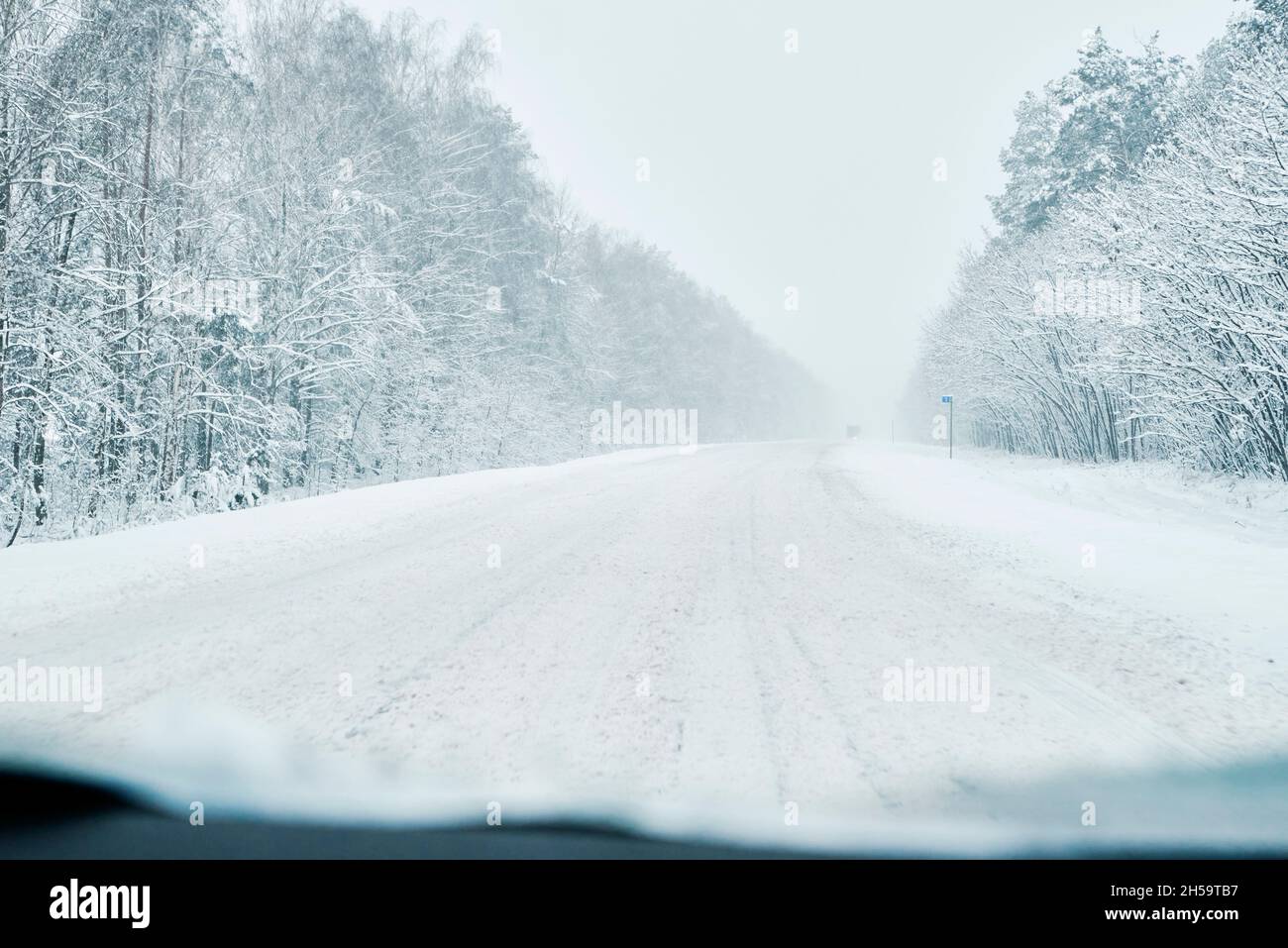 Winter forest with snowy road. Cars move on slippery road, dangerous ...