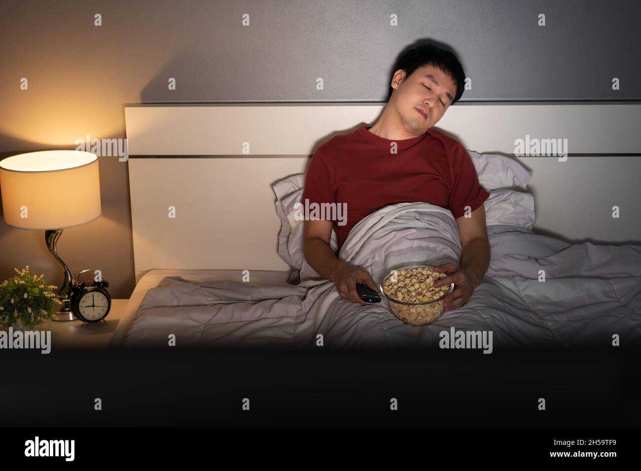 young man sleeping while watching tv on a bed at night Stock Photo Alamy
