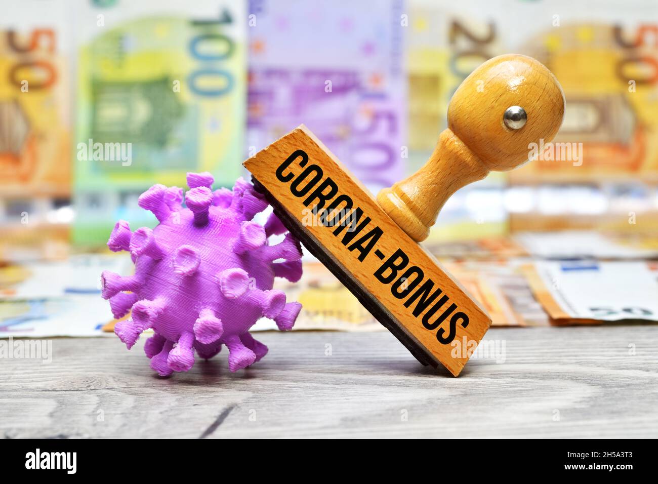 FOTOMONTAGE, Stempel mit Aufschrift Corona-Bonus und Coronavirus-Modell vor Geldscheinen Stock Photo