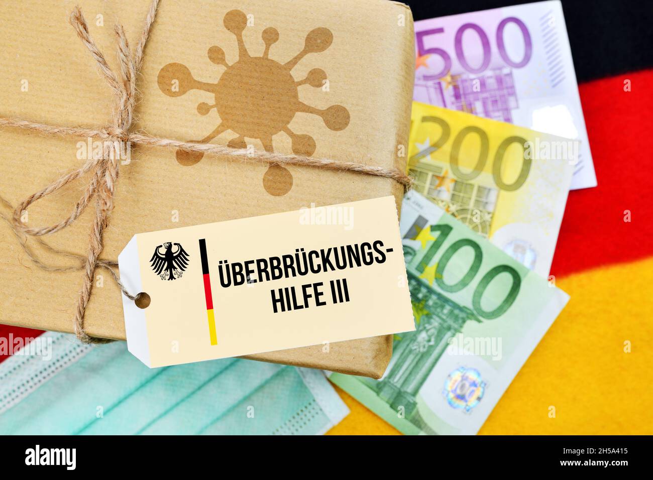 FOTOMONTAGE, Paket mit Coronavirus-Symbol auf Deutschlandfahne mit Etikett und der Aufschrift Überbrückungshilfe III Stock Photo