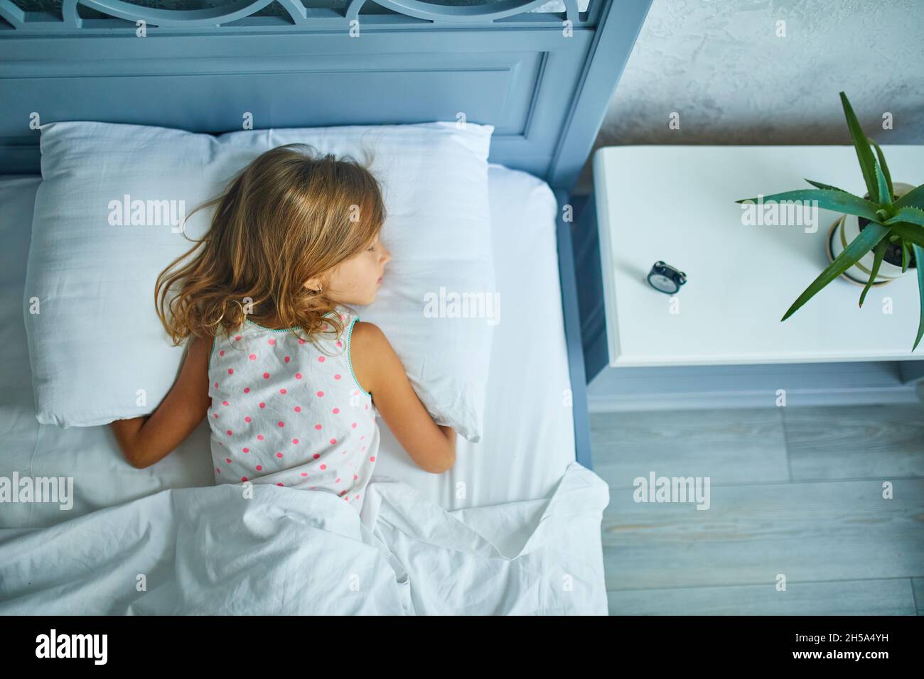Little girl sleeping on a big and cozy bed white linen in the afternoon ...