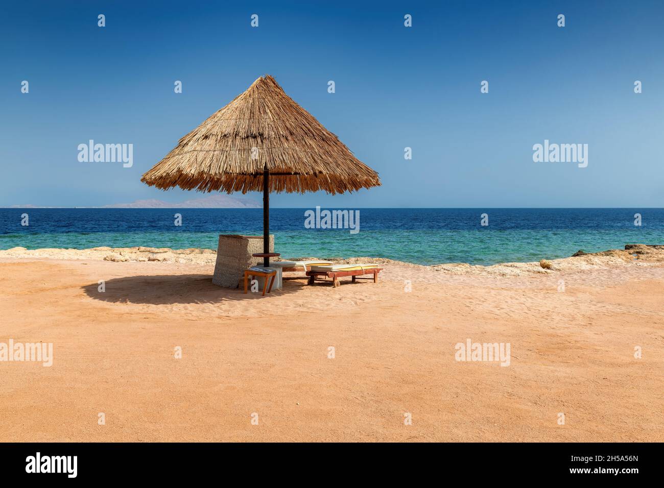 Sun umbrella and beach chairs in Sunny beach in tropical resort in in coral reef in Red Sea coast Stock Photo