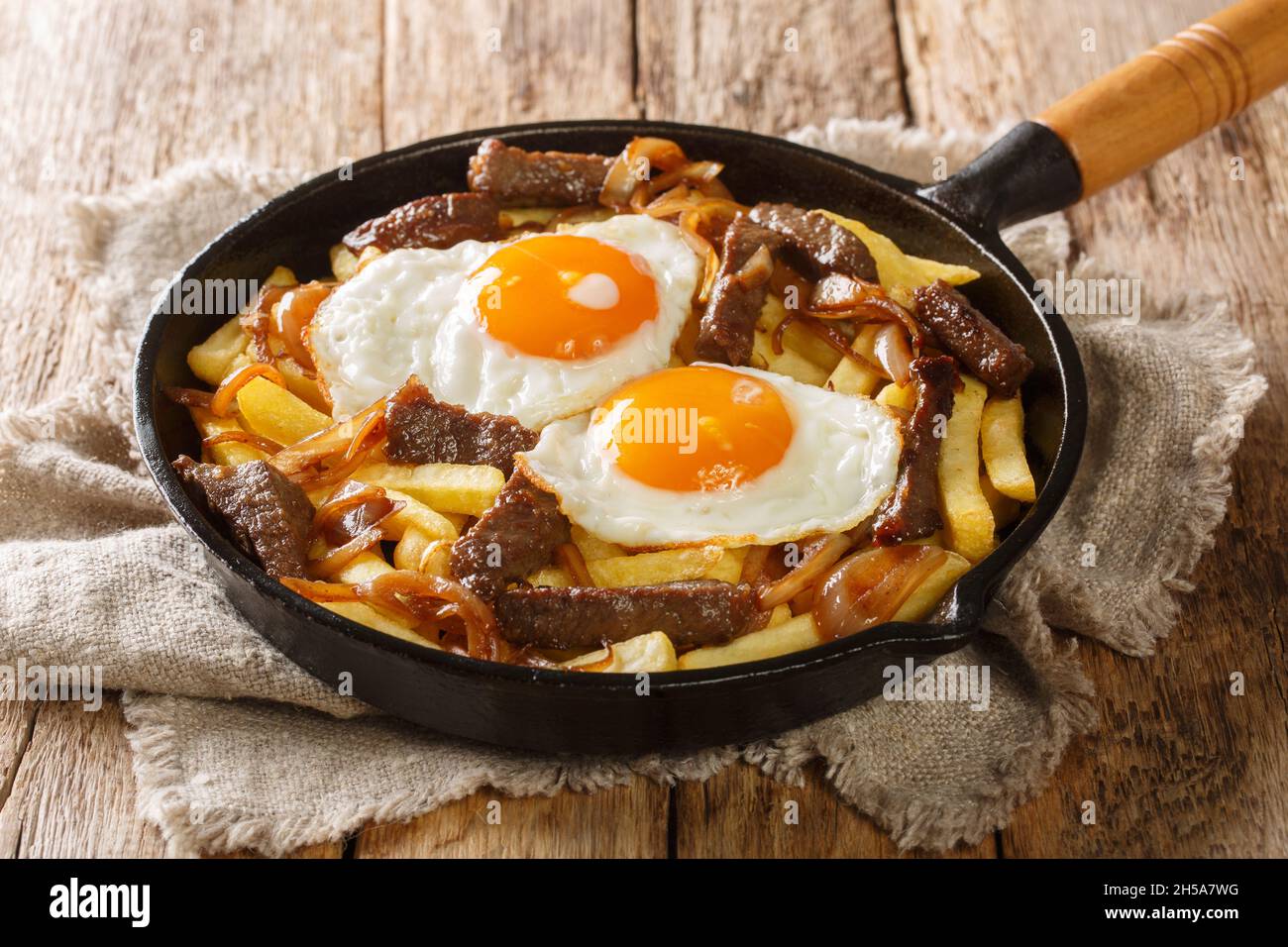 Chorrillana is a favorite Chilean dish of French fries loaded with beef, caramelized onions, and fried eggs close up in the pan on the table. Horizont Stock Photo