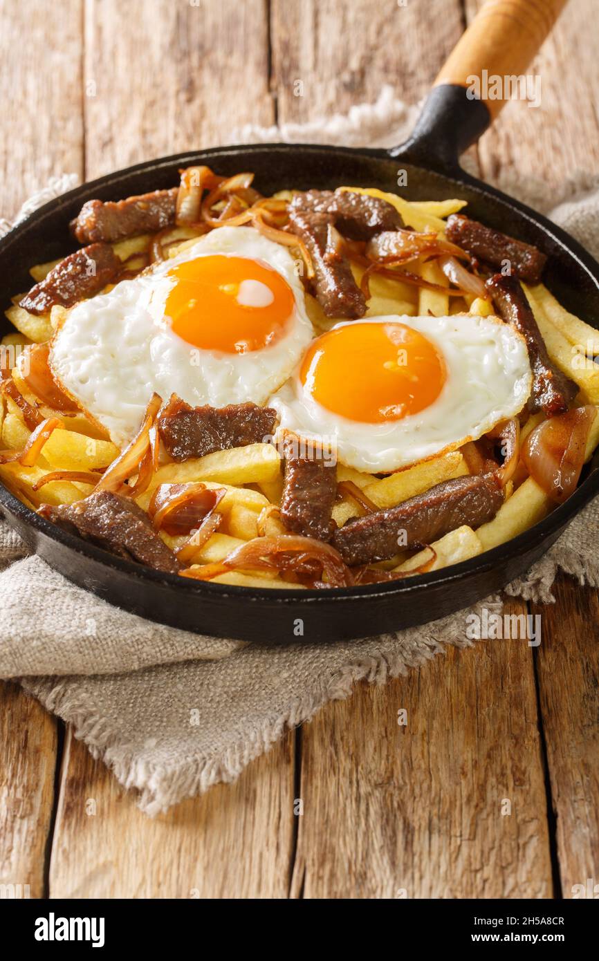 Chilean Chorrillana Fries with beef, caramelized onions, and fried eggs close up in the pan on the table. Vertical Stock Photo