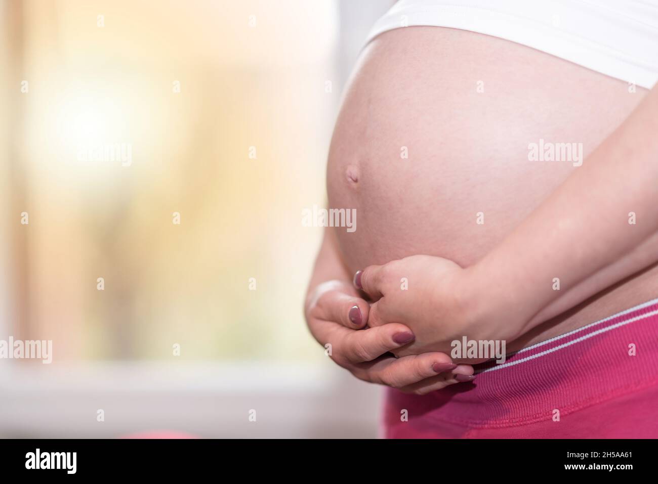 Pregnant woman holding hands on her belly Stock Photo - Alamy