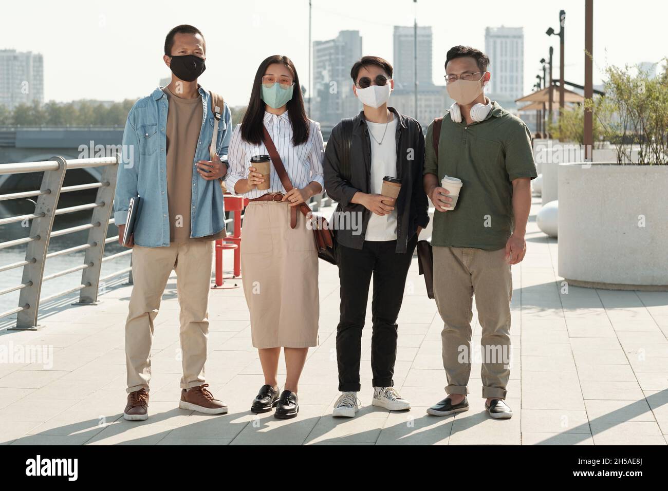 Line of four young Chinese white collar workers with drinks standing in front of camera against riverside and park Stock Photo