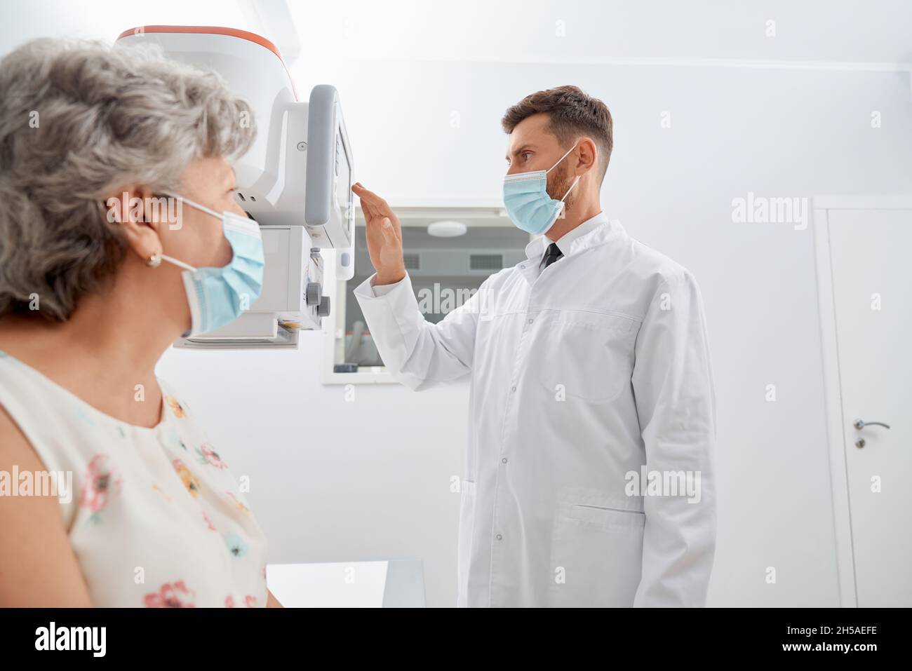 Side view professional radiologist touching screen of modern equipment starting scanning process. Old grey female patient waiting, examine health in modern clinic. Concept of medicine. Stock Photo