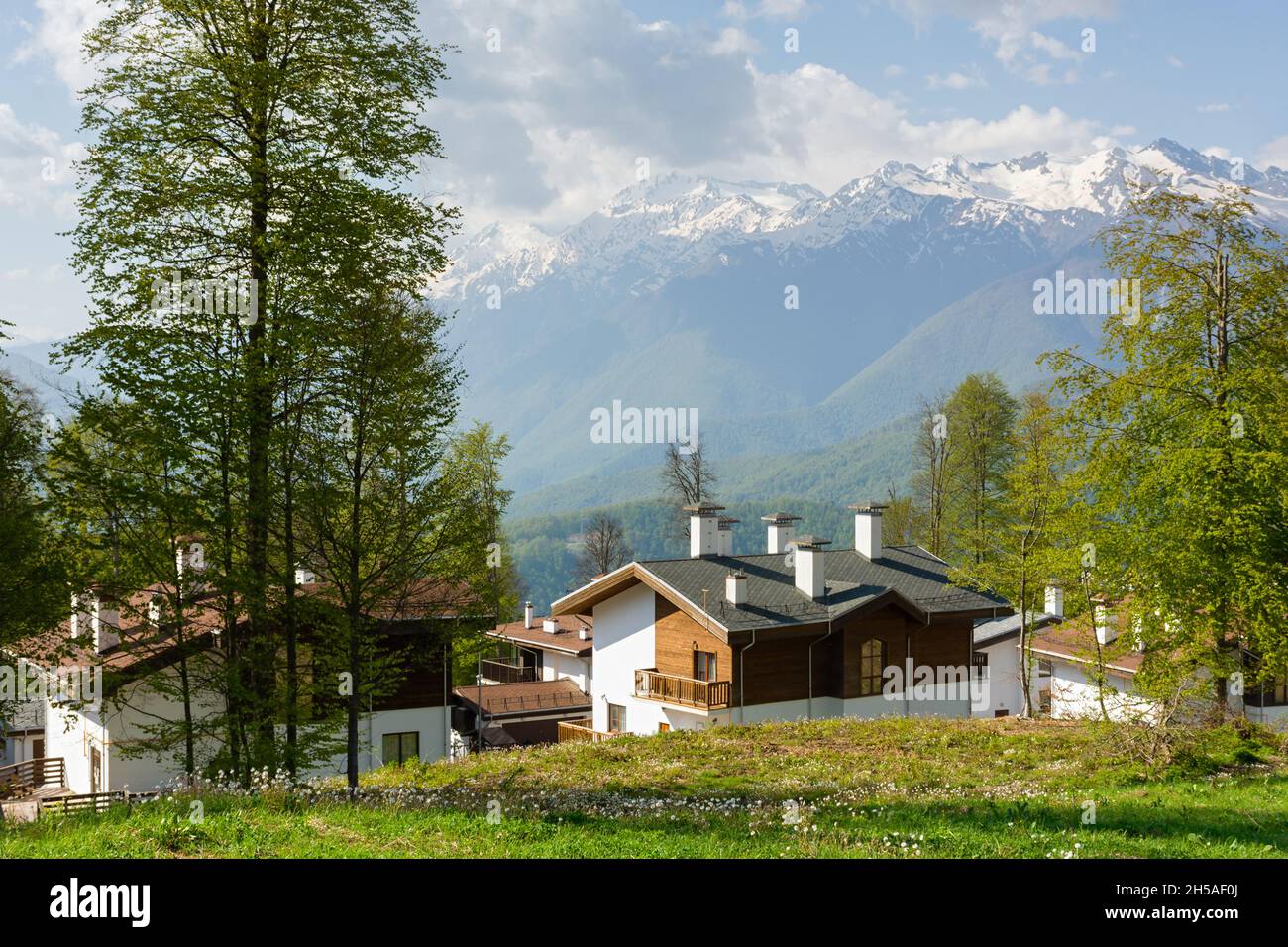Sochi Krasnodar Territory village of Rosa Khutor on April 29, 2018. View of wooden guest houses and mountains. Beautiful sunny spring landscape at a p Stock Photo