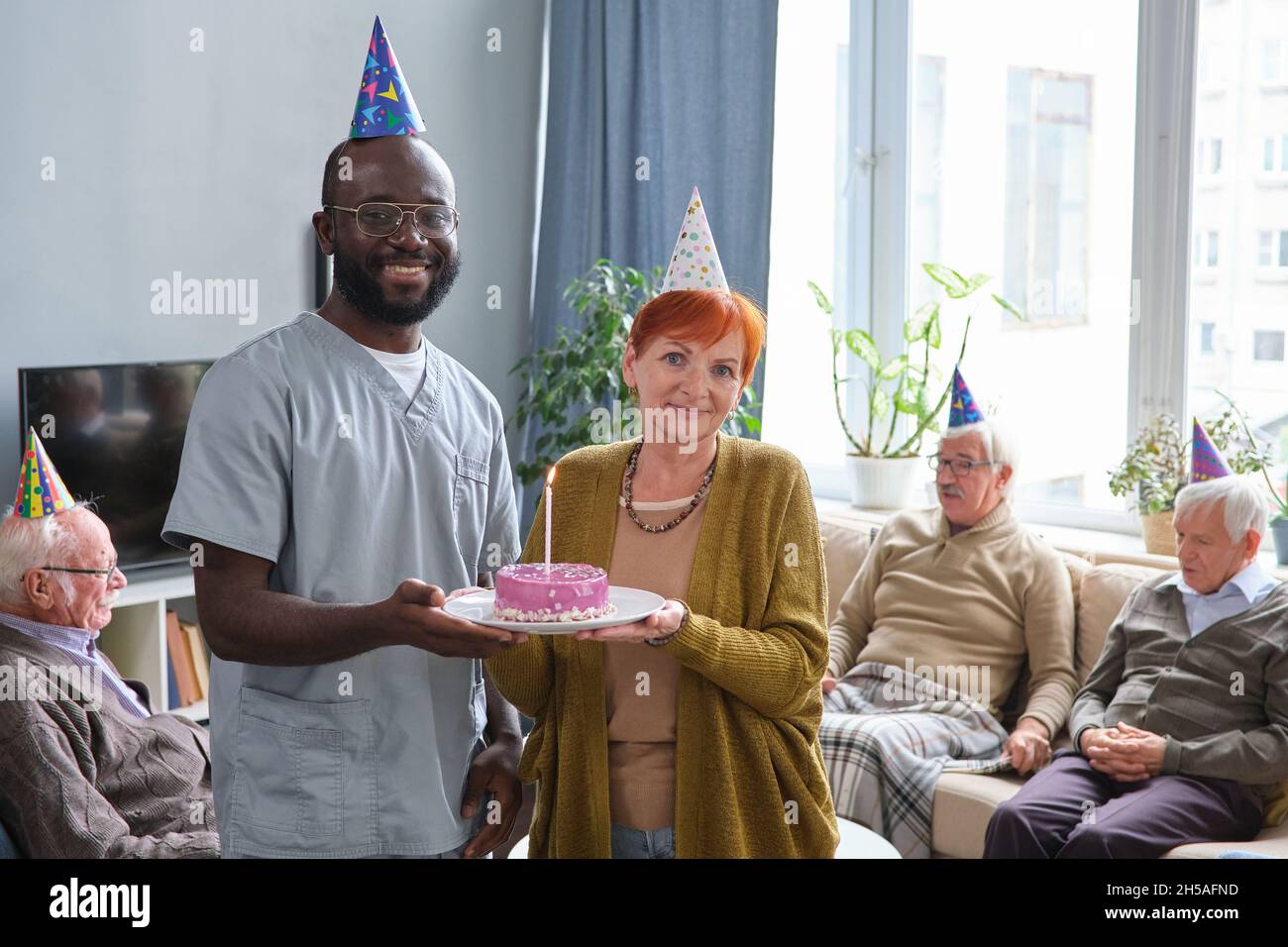 Portrait of African doctor smiling at camera while celebrating senior woman with birthday and giving a cake for her Stock Photo