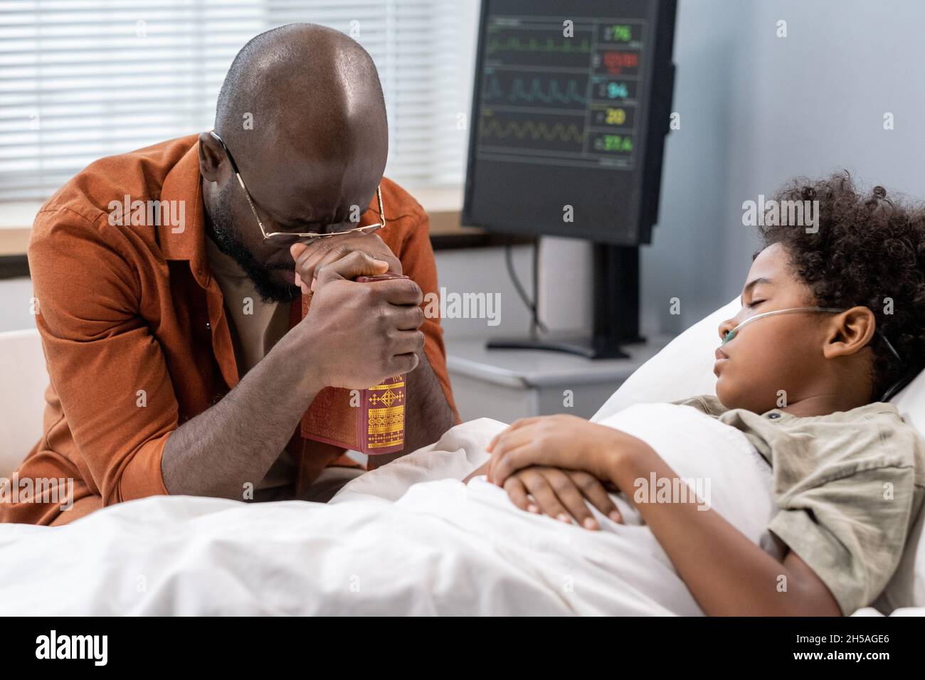 African father holding hand of his son and worrying about him while he lying in hospital bed Stock Photo