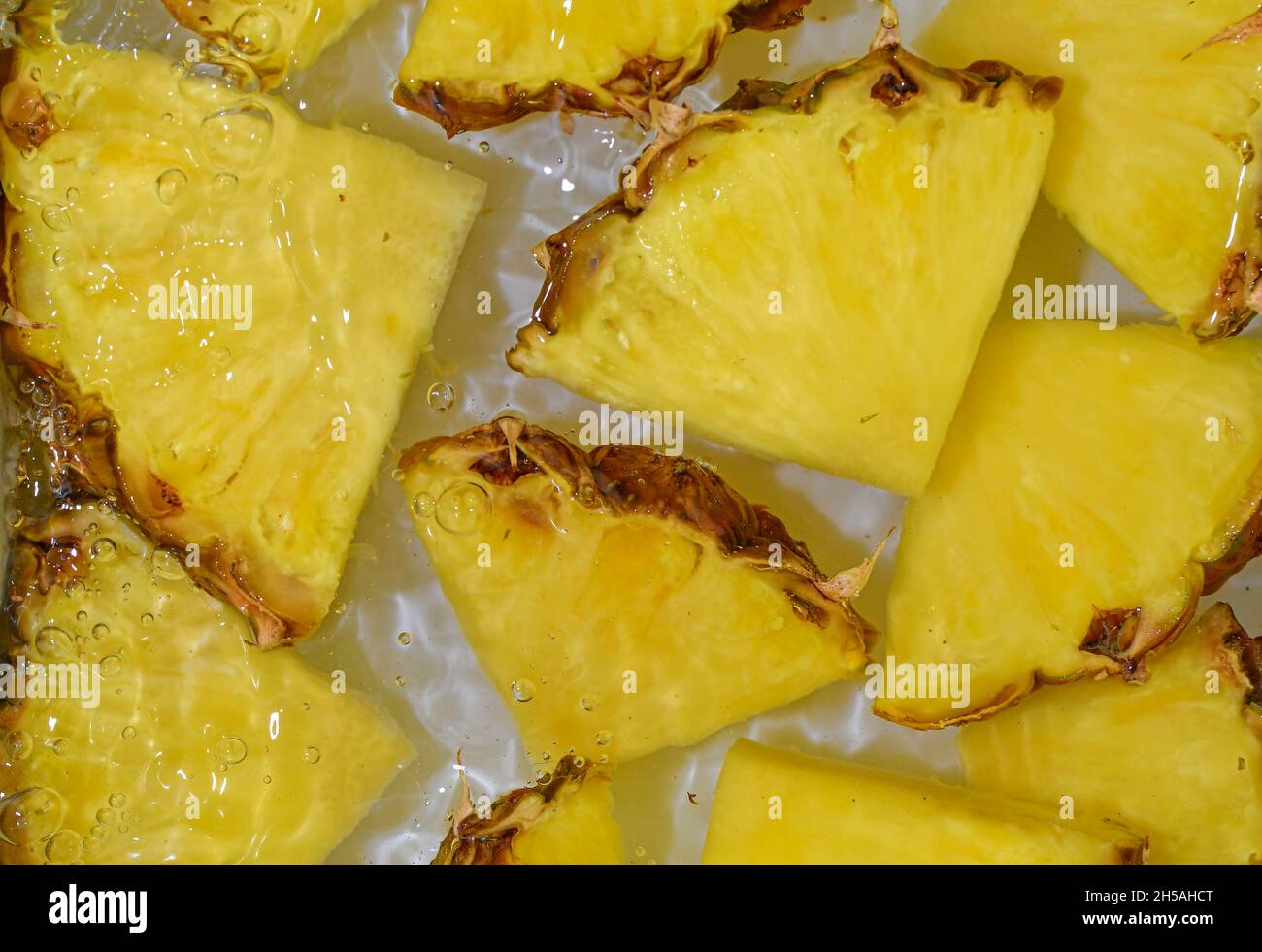 Close-up fresh slices of yellow pineapple on white background. Slices of pineapple in sparkling water on white background, close-up. Horizontal image Stock Photo