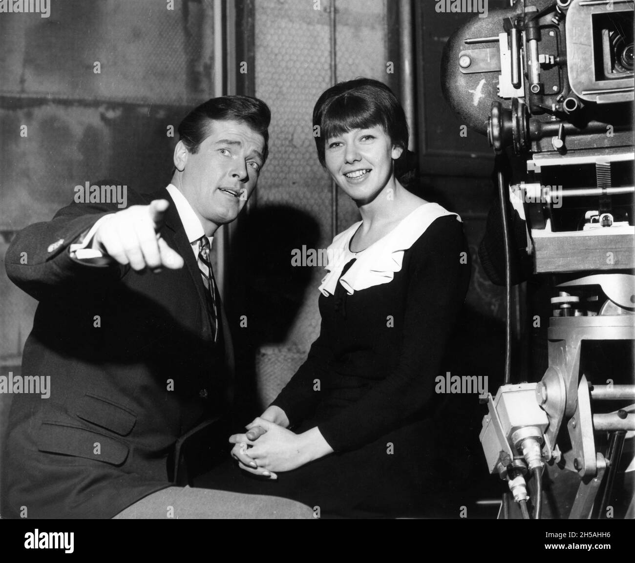 ROGER MOORE while appearing as Simon Templar on set candid at Associated British Elstree Studios with Unidentified Female Set Visitor / Fan during filming of THE SAINT TV Series circa 1965 writer Leslie Charteris music Edwin Astley producer Robert S. Baker Bamore / Incorporated Television Company (ITC) Stock Photo