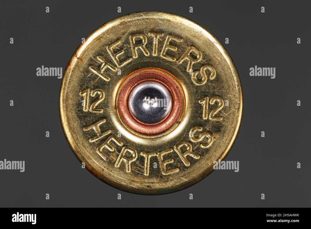 Bottom of a 12-gauge case with a pierced primer on a gray background. Macro photography Stock Photo