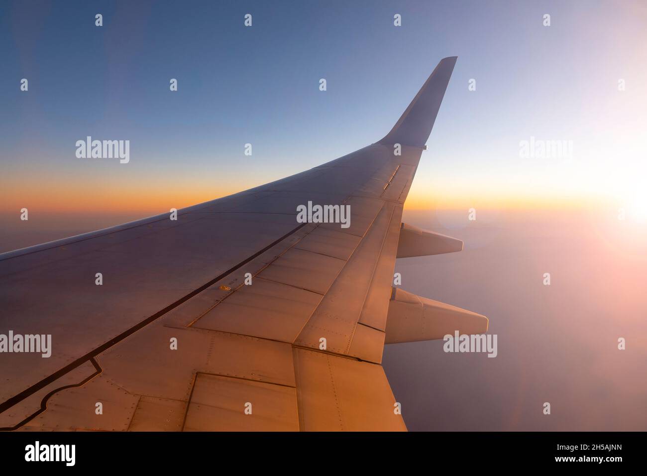Airplane flying above sky during sunset. Wing of the plane and sunlight Stock Photo