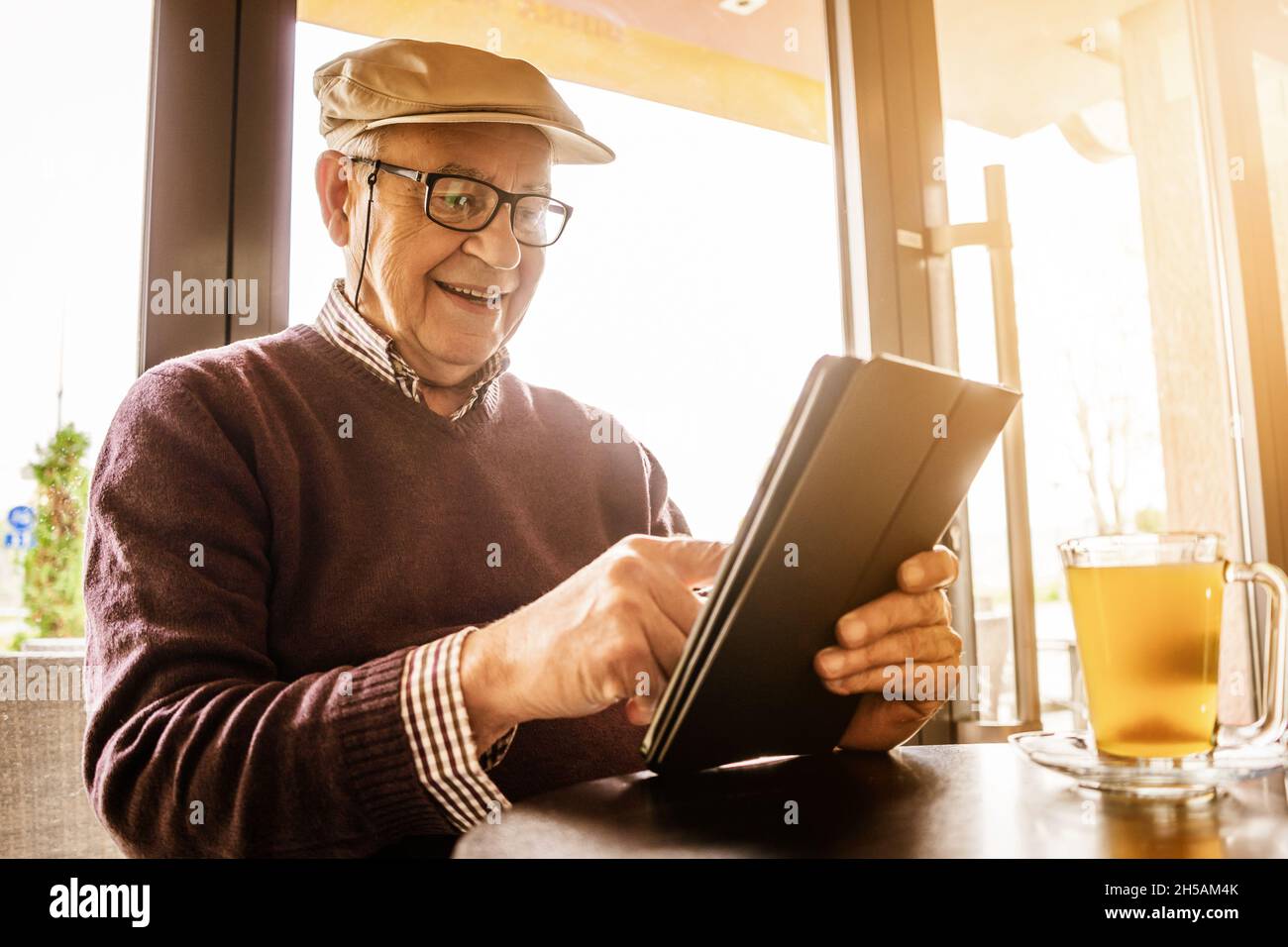 Senior man is sitting in cafe and using digital tablet. Stock Photo