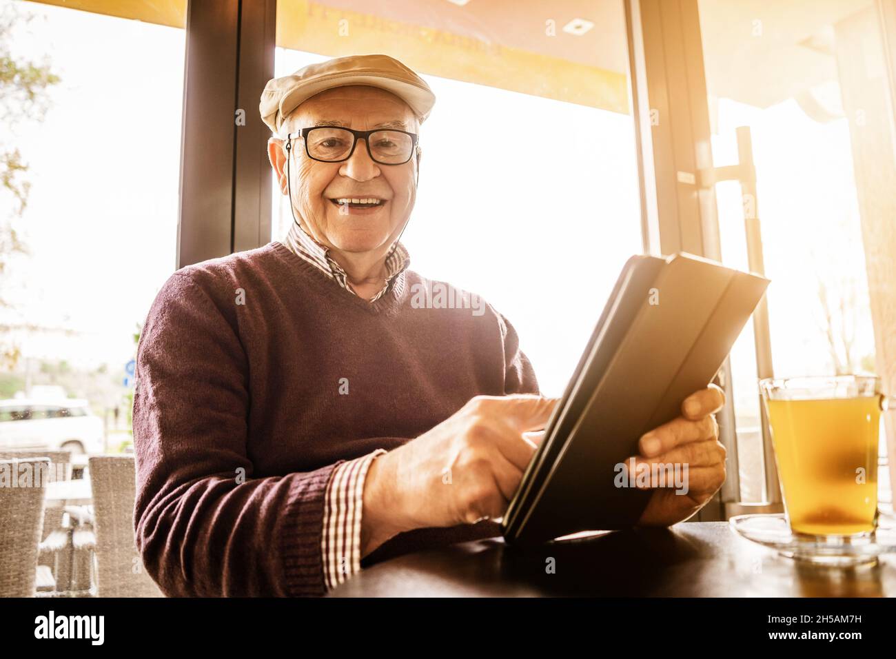 Senior man is sitting in cafe and using digital tablet. Stock Photo