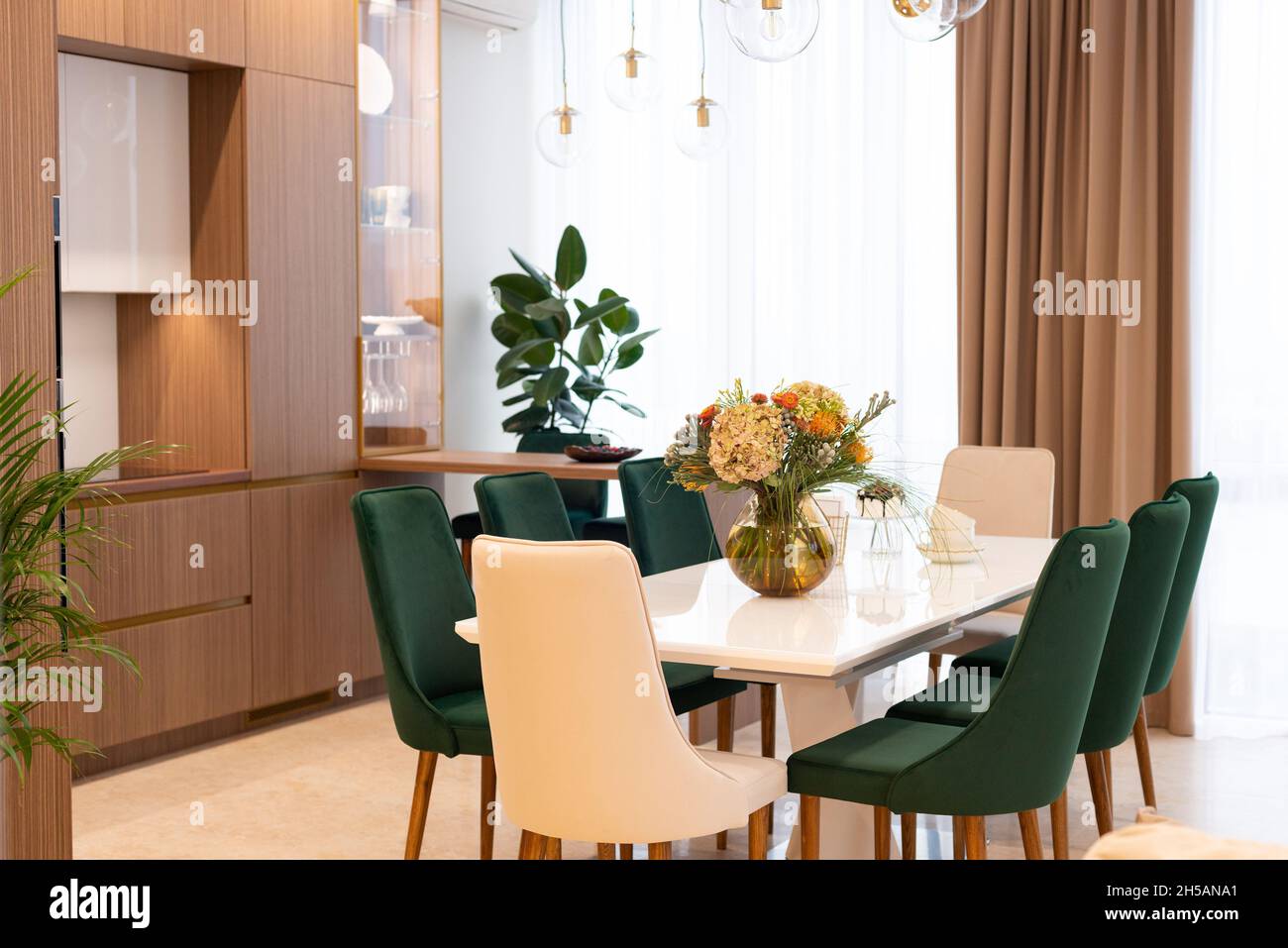 Modern dining room with cozy green and beige armchairs and a vase of flowers on a white table. Interior Design. Soft selective focus, artistic noise. Stock Photo