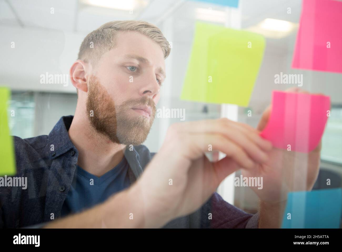 thoughtful businessman looking at sticky notes on window Stock Photo