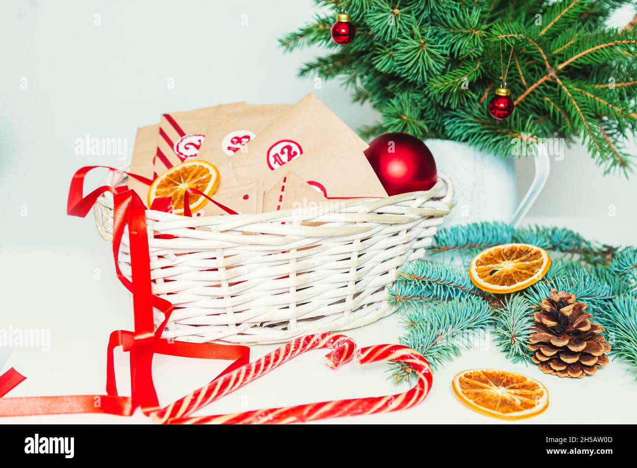 Advent calendar, fir branches and baubles. Kraft envelopes with numbers in a basket. Christmas tradition. Stock Photo