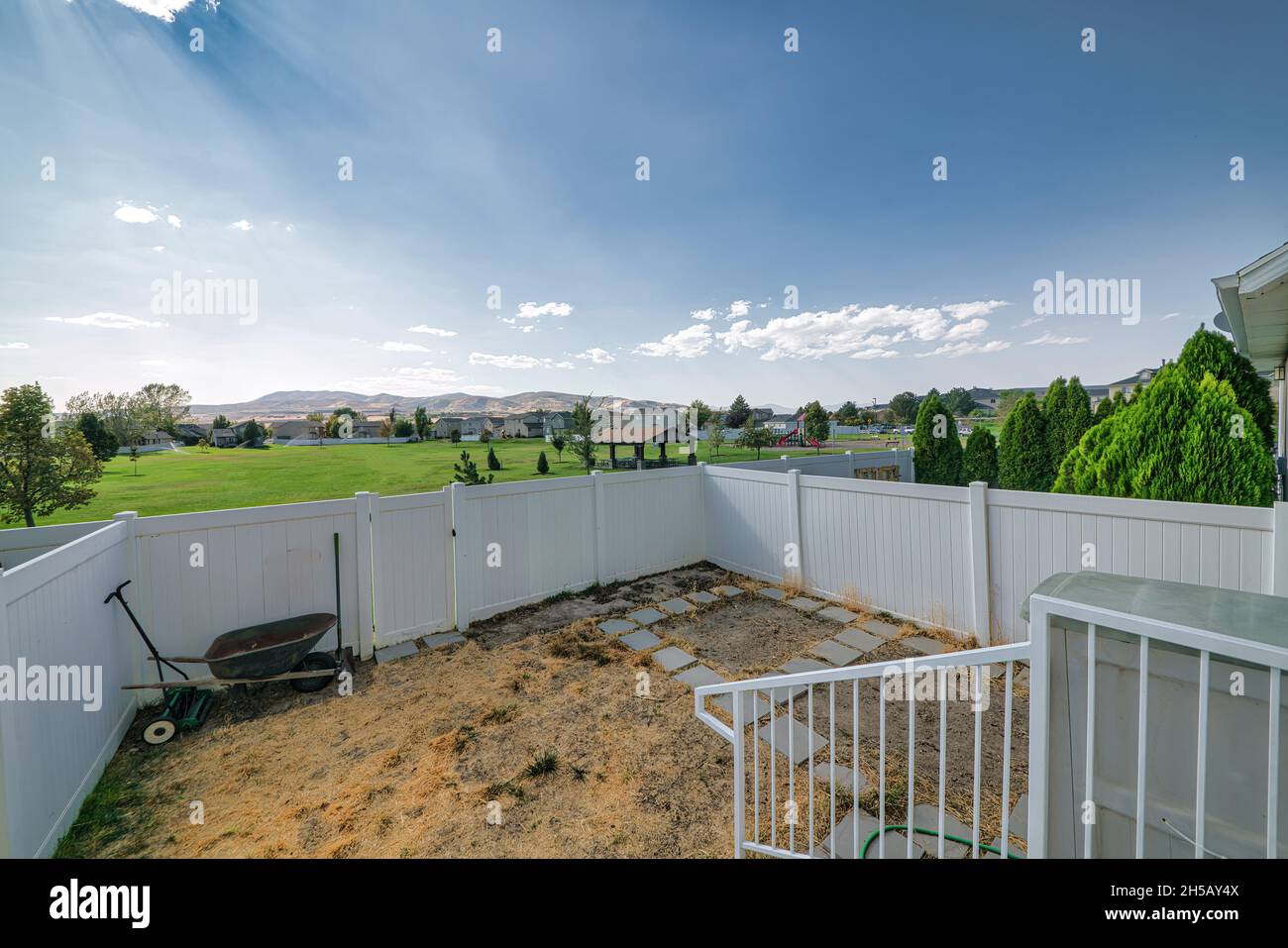 Backyard of a house with wheelbarrow, shovel and lawn mower against the white vinyl fence and gate. Stock Photo