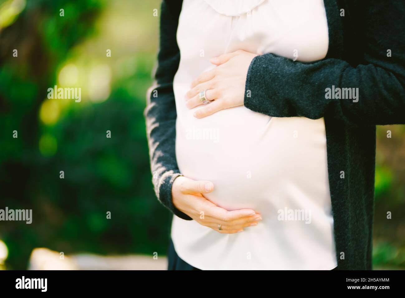 Pregnant woman hugs her belly with her hands while standing in the park ...
