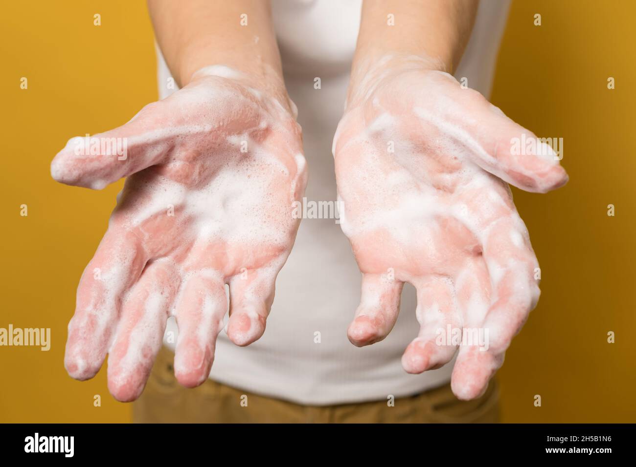 Woman shows her hands in soapy suds, on a yellow background. Concept for an effective way to prevent the spread of infections. Close-up. Stock Photo