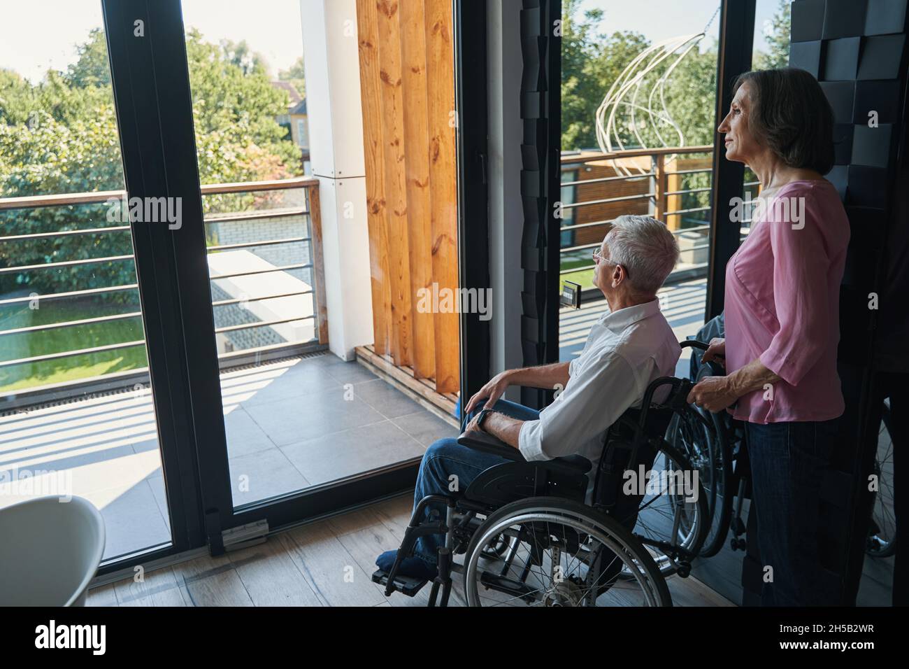 Man with disability in wheelchair looking at yard from window Stock Photo