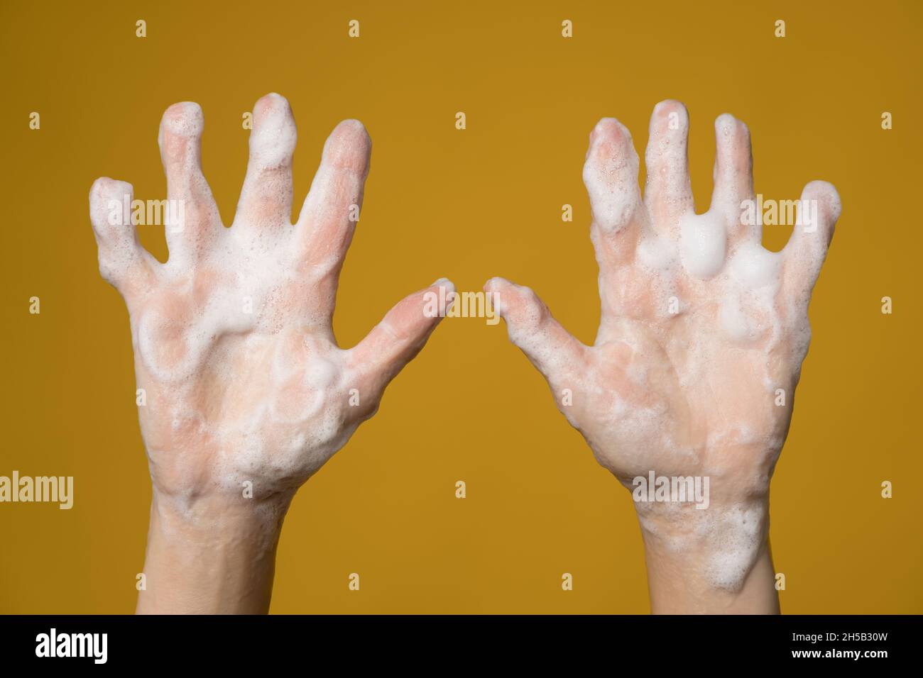 Hands covered with soapy foam. Isolated, on a yellow background. Concept for an effective way to prevent the spread of infections.  Stock Photo