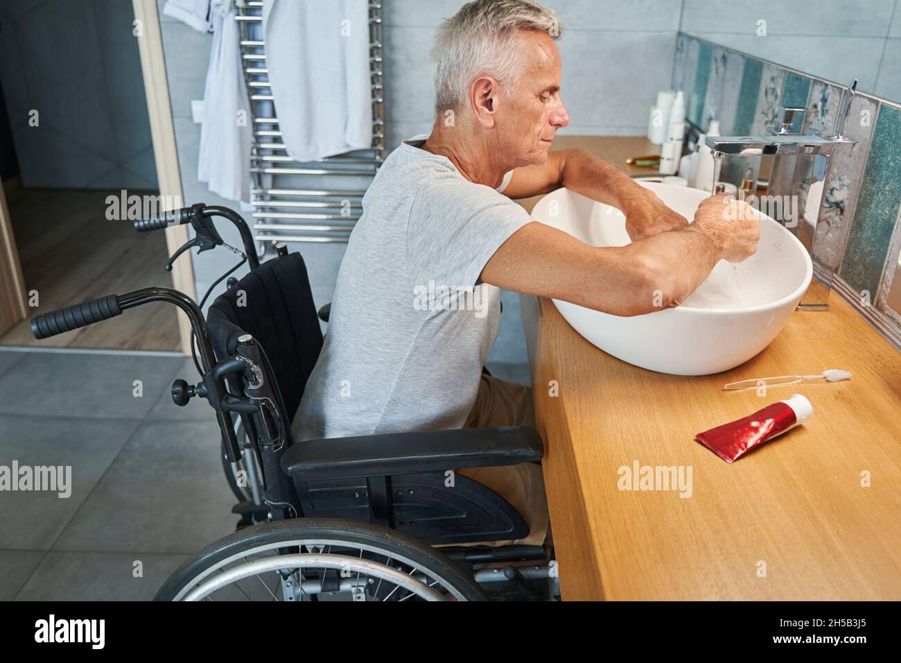 Aged man with physical disability cleaning hands in sink Stock Photo