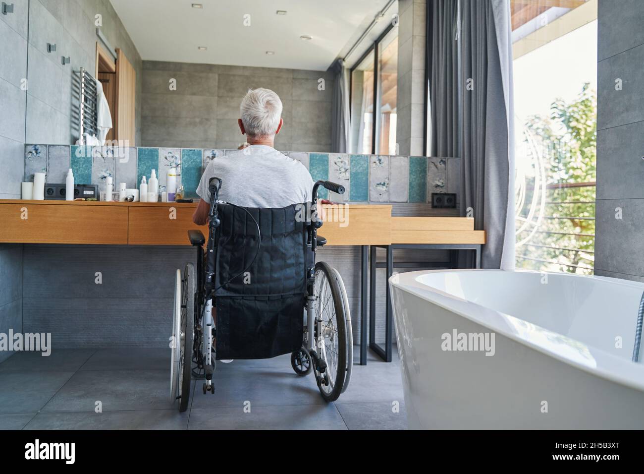 Back view of old man in wheelchair before bathroom mirror Stock Photo