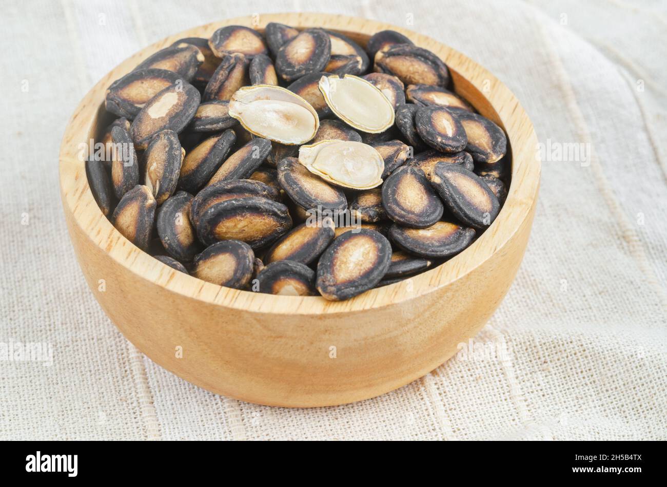 Black dry watermelon seeds in wooden bowl on the tablecloth. Stock Photo