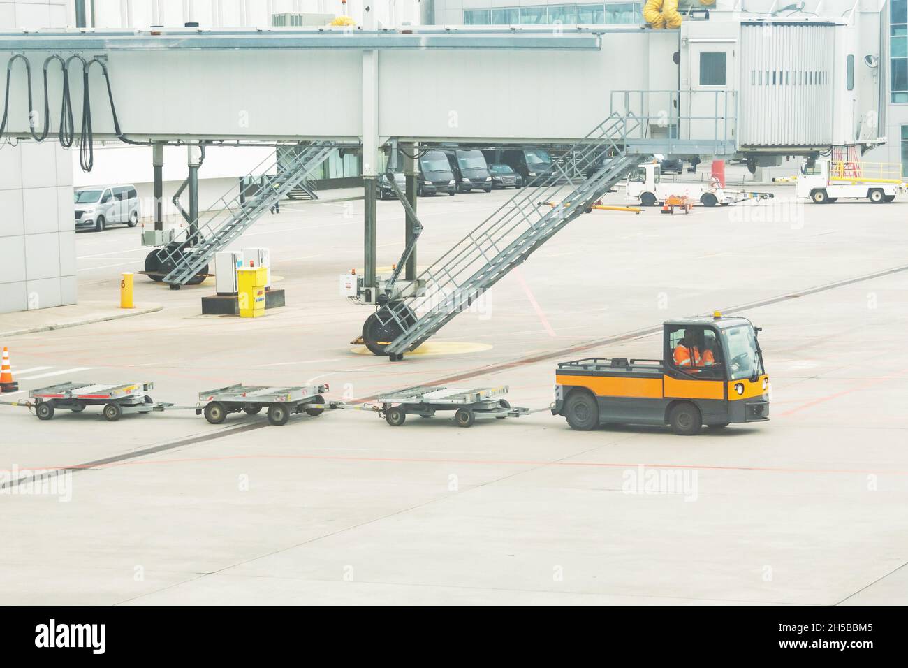 Several empty luggage trolleys are transported to the plane for unloading flight bags, against the background of the boarding bridge gangway of the te Stock Photo